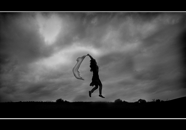 Silhouette of a person jumping while holding a transparent cloth against a backdrop of stormy clouds - purposefully breaking the rules of photography by having a centered subject, shooting against the light, and the image being heavily underexposed.