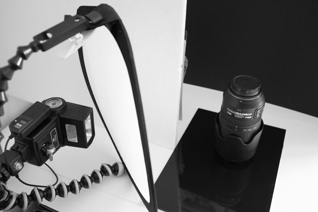 Setup for creating a low key photo of a camera lens, with a piece of polystrene used to block the light from hitting the background. (A piece of black card would have been more suitable but the polystyrene was convenient).