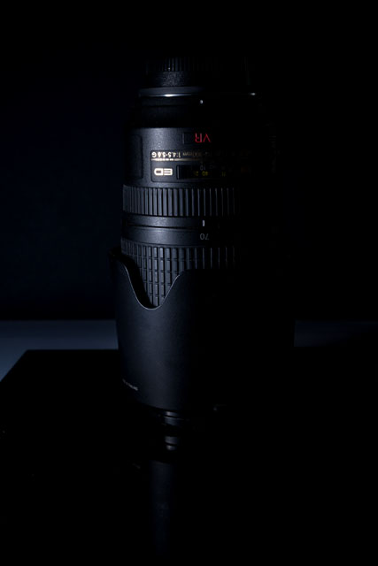 Low key photo of a camera lens, light from the flash has spilled onto the surface behind the subject a bit
