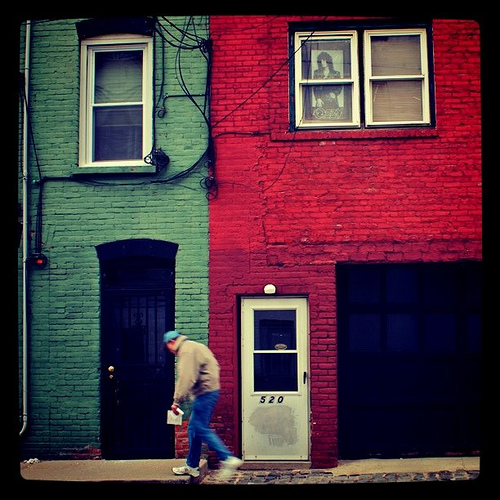 Street photography with a camera phone - man walking past brightly colored houses with a poster in the top window