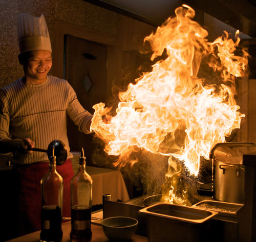 Man cooking, flames jumping up from a hot wok
