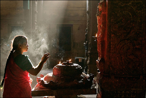 Woman praying in Meenaskshi temple, Madurai. Atmospheric lighting emphasizing smoke from incense.