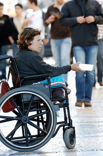 Lady in a wheelchair begging as people walk by