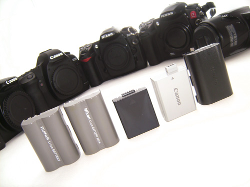 Different camera batteries with the cameras they come from in the background