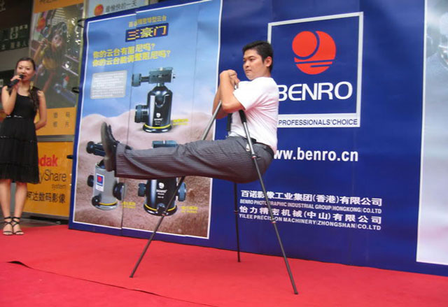 Man hanging from a tripod at a demonstration by tripod manufacturer Benro