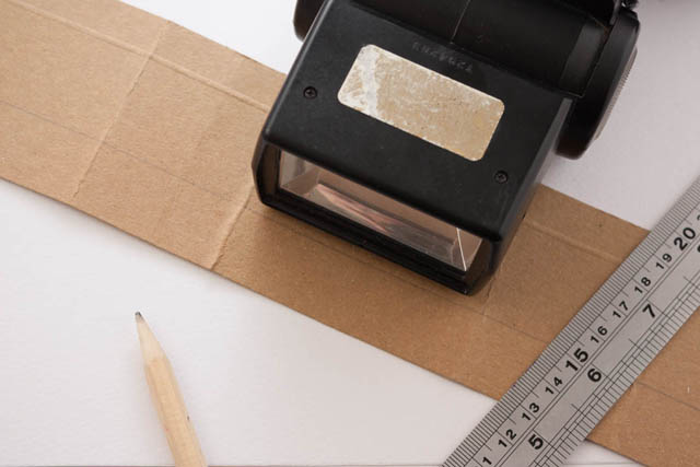 Speedlight flash on strip of cardboard with ruler and pencil for marking and bending the card