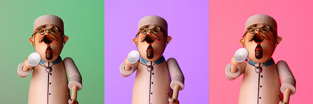 3 photos of a wooden model of a doctor, each with a different background color. The background color was changed by lighting it using different colored gels with a speedlight flash.