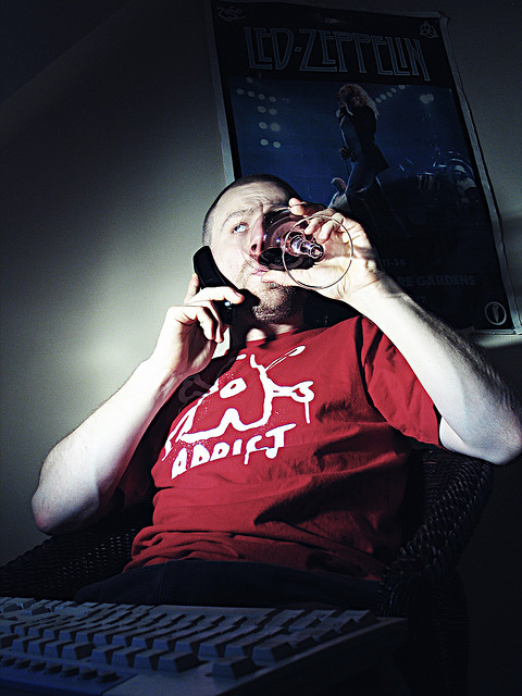 Portrait of a man drinking a glass of wine while on the phone, sitting behind a computer. The portrait was lit with a flash that only goes down to 1/16th power so an ND flash gel was used to further reduce the power of the flash to the desired level.
