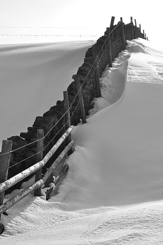 Wall leading over a snow covered hill against a white sky