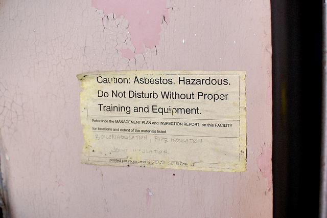 Asbestos warning sign and peeling faded red paint