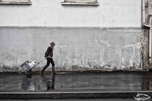 Woman pulling a crate along the street, the photo has a wide range of tones from black to white and has a standard level of contrast