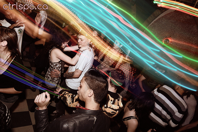 Dancers at a club with bright lights sweeping across the image due to use of moving the camera during a slow exposure while using flash to keep the people sharp