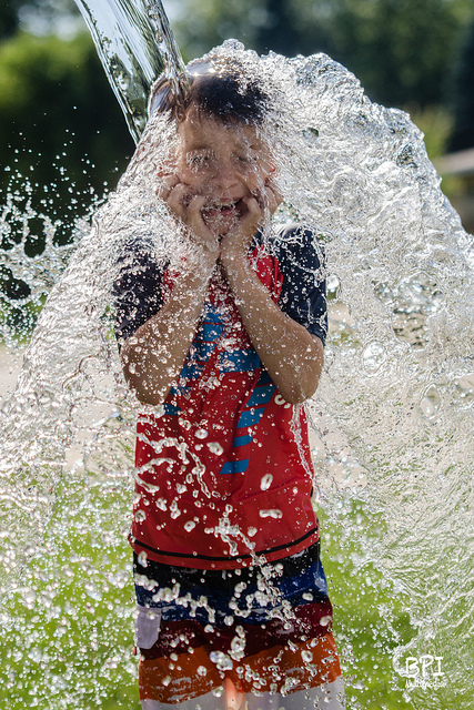 High speed photo of a boy being splashed with water, taken outdoors on a sunny day and using high speed sync flash